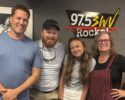 Four smiling adults stand together in a radio studio, with a soundboard in the foreground and a 97.5 SWV Rock logo on the wall behind them.